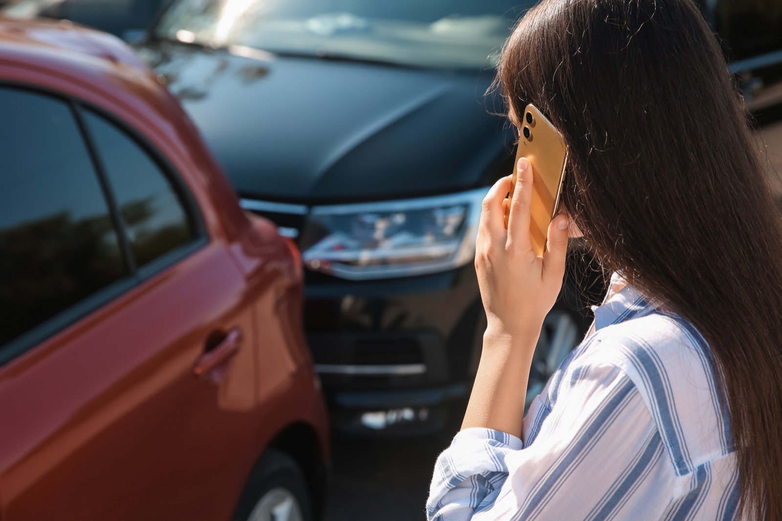 事故で接触した車の前でスマートフォンを耳に当てる女性