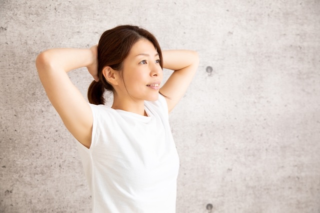 頭の後ろで手を組み、両肘を横に開いて立つ女性