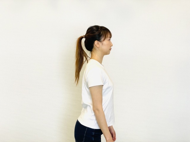 白いTシャツで背すじを伸ばし、真横を向いて立つ女性