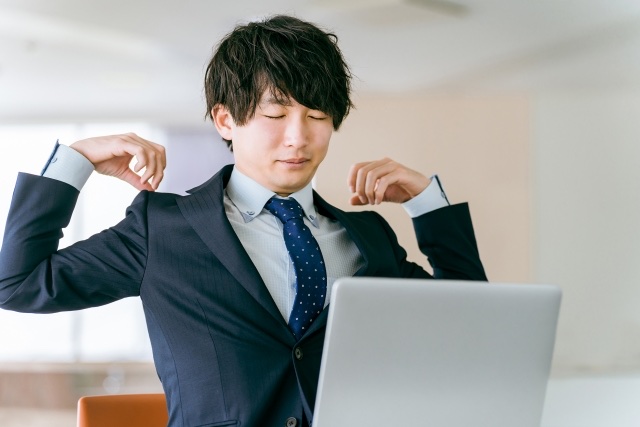 ノートパソコンの前で指先を肩に当てて肩を回す男性
