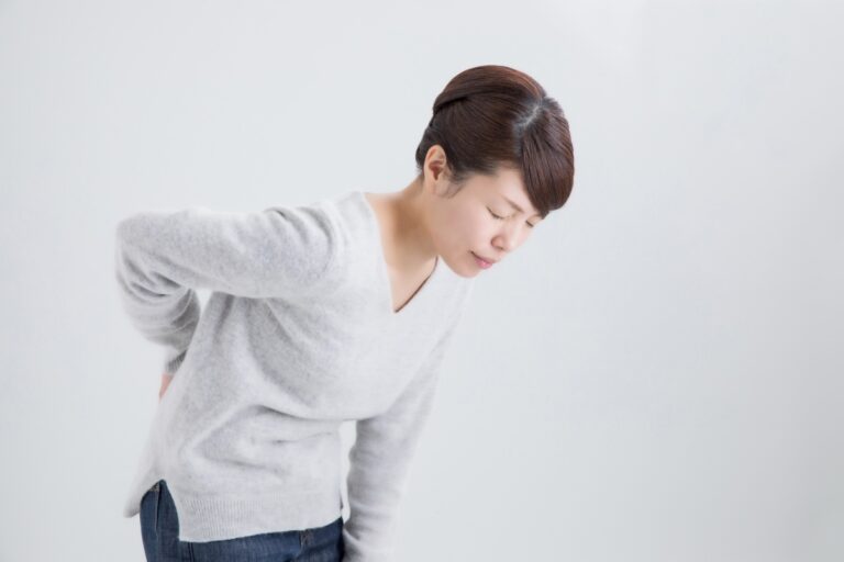 グレーのニットの女性が前かがみで腰に手を当てる
