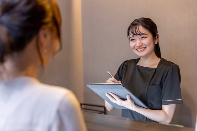 受付でタブレットを持ち笑顔で話を聞く女性スタッフ