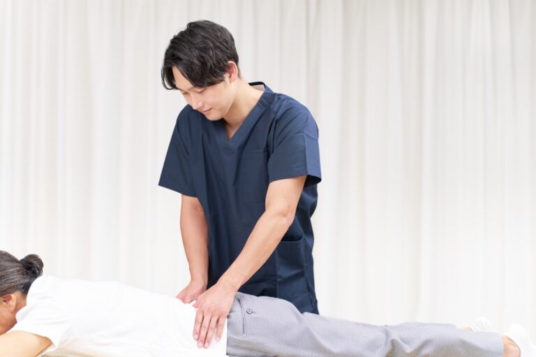 紺の術衣の男性がうつぶせの女性の腰に両手を当てる