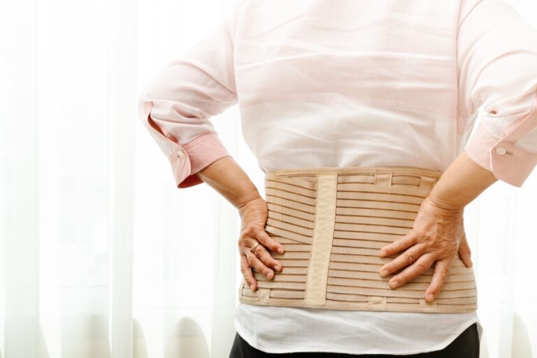 腰にベージュのコルセットを巻き、両手を当てる人の後ろ姿