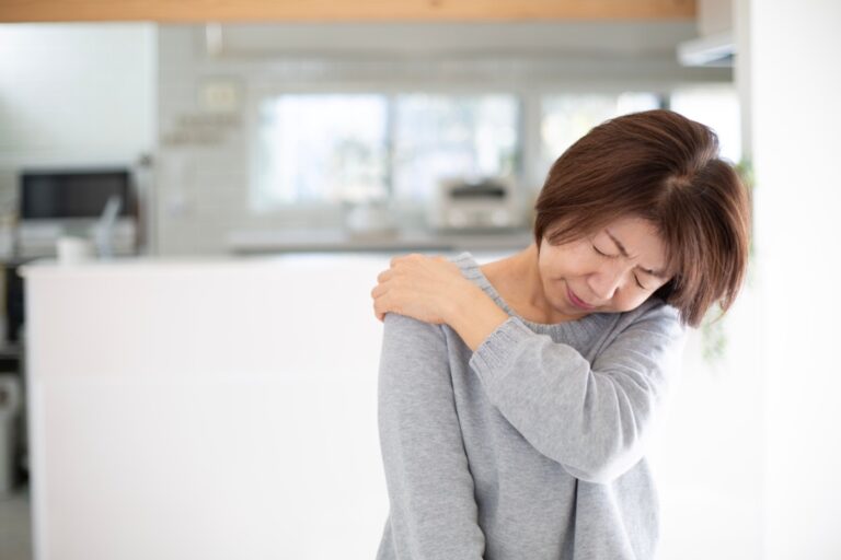 キッチンを背に顔をしかめて肩を押さえる女性